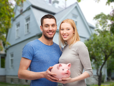 smiling couple holding piggy bank over house